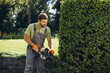 © Petro - Man worker cutting bushes with an electric saw in the yard