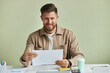 © Seventyfour - Minimal portrait of smiling bearded man at desk looking at camera against pastel green wall in office