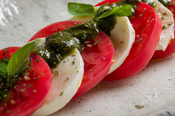 Poster - Caprese salad with mozzarella cheese, tomato, basil and sauce pesto on plate on marble table extreme macro close up