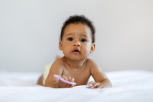 Portrait Of Little Black Baby Lying On Bed With Teether In Hand