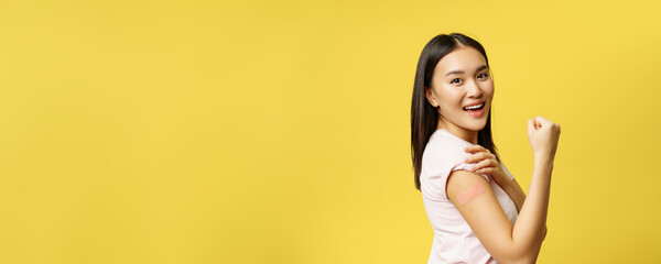 covid-19 and healthcare medical concept. cheerful asian girl shows arm with patch after coronavirus 