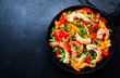 Leinwanddruck Bild - Stir fry with shrimps, red and yellow paprika, green pea, chives and sesame seeds in frying pan. Asian cuisine dish. Black stone kitchen table background, top view