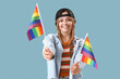 Beautiful young woman with LGBT flags on blue background