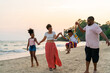 © CandyRetriever  - Happy African family on summer holiday vacation. Father, mother and little kid walking together on the beach at sunset. Parents and children enjoy and fun outdoor lifestyle playing together at the sea