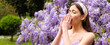 Spring allergy, flu. Banner. Sick woman sneezing covering nose with a wipe in a park. Spring allergy concept. Fashionable youth style. Allergic people. Among blooming trees and flowers in park.