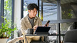 © bongkarn - Happy and relaxed Asian an using his phone and portable tablet at the coffee shop. remote working