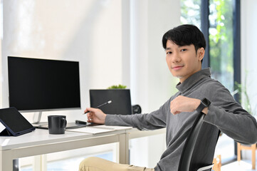 Wall Mural - Handsome Asian male graphic designer or program developer sits at his desk in modern office