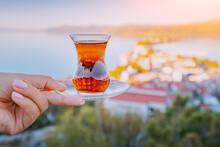 Delicious And Fragrant Turkish Tea In A Traditional Authentic Bardak Glass In The Hand Of A Tourist Against The Backdrop Of A Resort Town