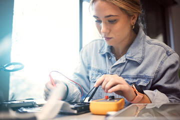 Engineer, student and woman repair electronics for science project. Learning, education and female technician with technology testing microchip, gadget or circuits for electricity with electric meter