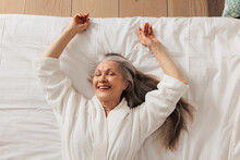 Happy Aged Woman In A Bathrobe Lying On A Bed With Closed Eyes