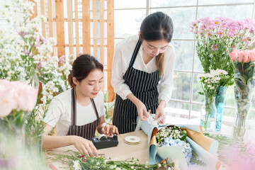 Two Asian female florists preparing and arranging and wrapping bouquet flowers at flower shop. Small business owner, entrepreneur