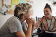 © Maskot - Smiling mental health professional looking at female student sitting with hand on chin in school office