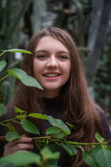 Wall Mural - Portrait of happy beautiful young science student. Youn girl in a greenhouse with tropic plants. She is studiing plants