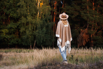 Woman wearing poncho and cowboy hat outdoors. Boho fashion style