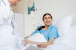 © LIGHTFIELD STUDIOS - Cheerful patient in gown lying on bed near blurred doctor in clinic.
