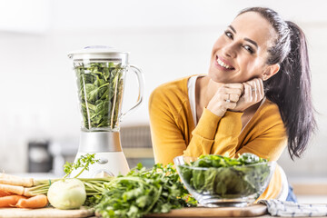 Wall Mural - A young woman prepares an energy drink from fresh vegetables using a blender.