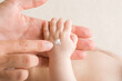 Young adult mother finger applying white moisturizing cream on newborn hand. Care about baby clean and soft body skin. Closeup.
