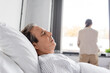 © LIGHTFIELD STUDIOS - Senior man lying on bed near blurred daughter in hospital ward.