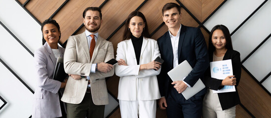 heterosexual multi national office staff with a smile looking at the camera standing against the wall