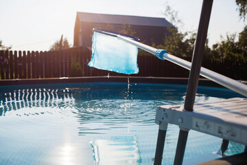 Cleaning a swimming pool with a metal frame with a net from leaves and dirt. Pool cleaner during work. Solar banner. The concept of summer holidays.