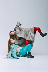 Portrait of two young women in bright red and blue tights and coat posing over grey studio background. Uniqueness. Vivid style, queer, art, fashion