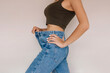 Cropped shot of a young slender woman dressed in wide jeans and top demonstrating successful weight loss isolated on a light beige color background. Diet and wellness concept