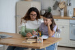 © DimaBerlin - Diligent pensive teenage girl sits next to mother helping to complete tasks of school teacher. Caring attentive millennial woman sits with daughter at kitchen table with textbooks and notebooks