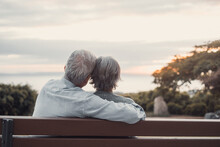 Head Shot Close Up Portrait Happy Grey Haired Middle Aged Woman With Older Husband, Enjoying Sitting On Bench At Park. Bonding Loving Old Family Couple Embracing, Looking Sunset..