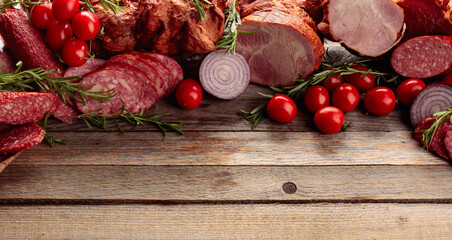 Wall Mural - Salami, ham, fresh sausages, tomato, and rosemary on an old wooden table.