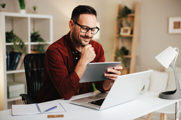 Young man works in the office at a desk with a tablet and a laptop