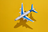 Fototapeta Boho - Toy plane flying on a yellow background with a shadow. Travel concept. Top view