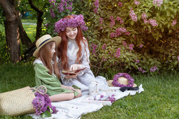 two sisters with long red hair at a picnic in a lilac garden