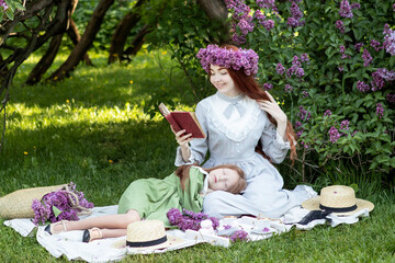 two sisters with long red hair at a picnic in a lilac garden