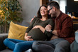 © Dorde - Expectant parents sitting on a sofa dreaming about their baby. Happy husband hugging his pregnant woman in a living room at home.