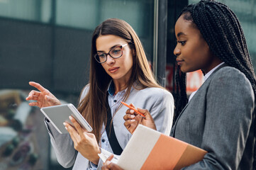 Two multiracial business woman meeting outside and using a tablet