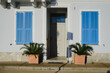 Grey facade of the house with a door, blue wooden shutters and potted flowers