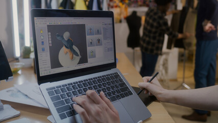 Female fashion designer develops future design of clothes in 3D modeling program on laptop using digital tablet and stylus. She works in atelier workshop. Fashion and technologies in business concept.
