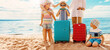 © candy1812 - Mother and father with their children standing on the beach with suitcases.