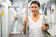© JackF - Asian woman with shoulder bag standing in subway train, holding handrail and looking in camera.