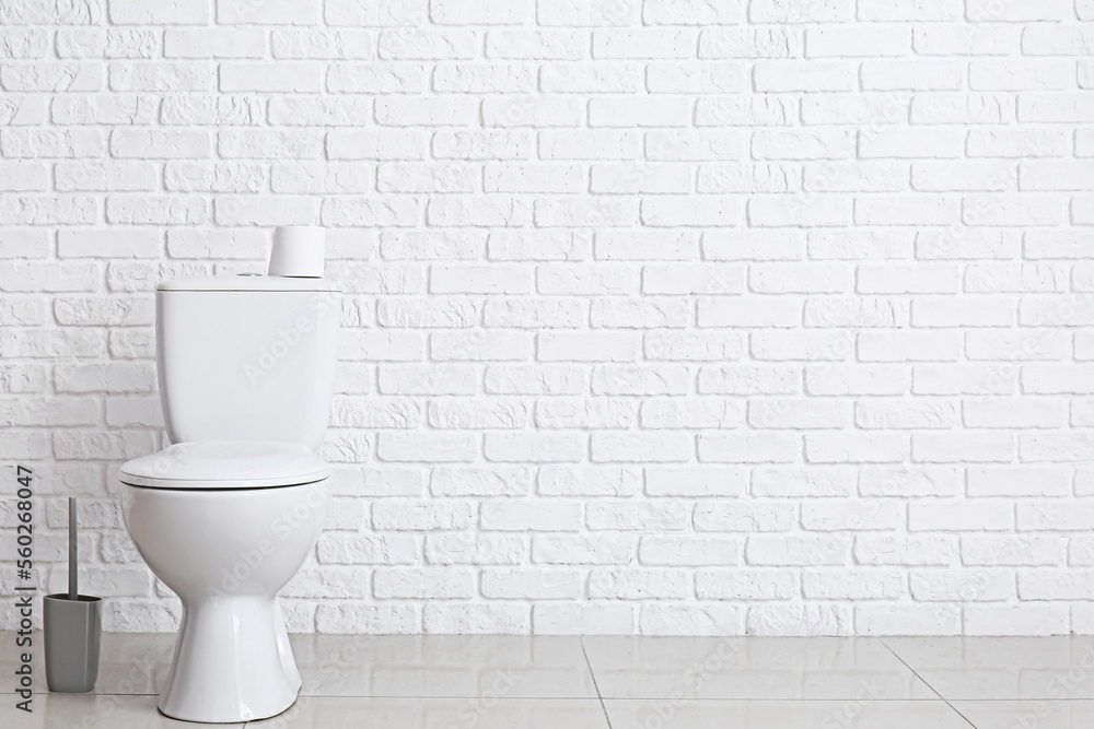 Modern toilet bowl near white brick wall