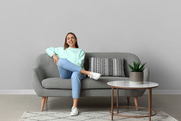 Young woman sitting on soft couch near grey wall