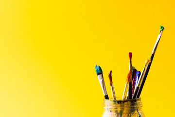 Image of close up of jar with paint brushes and copy space on yellow background