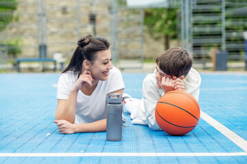 Wall Mural - Teenage boy and girl are sitting on sports field, drinking water and talking during break.