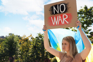 Wall Mural - Sad woman holding poster with words No War and Ukrainian flag outdoors