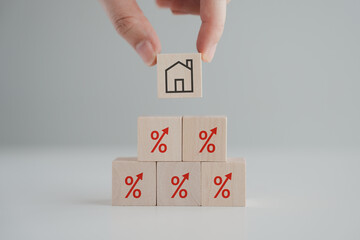 Hand holding house icon on wooden block from red percentage sign with arrow up. Refinance, Interest rates increase, Home loan, Mortgage, House tax. Property investment and asset management concept.