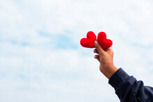Young Girl Holding A Heart On Blur Sky Background. Valentine Day, The Child's Hand Gripped The Red Heart, Lifting It Into The Sky.