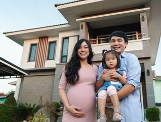 Wall Mural - happy family standing outside house, husband and pregnant wife and baby girl