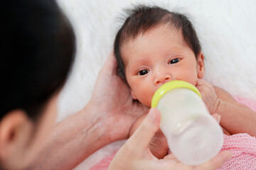 Wall Mural - mother feeding milk bottle to her newborn baby on bed