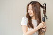 © KMPZZZ - Beautiful curly brunette, attractive asian young woman, girl smiling using curler, curling iron long hair with ceramic curler straightener at home. Hairstyle and Hairdressing. Beauty and hair care.