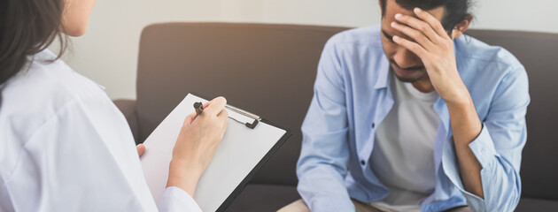 Asian young man, male has mental symptoms which must have been therapy and stress, sitting on couch, counseling with psychologist during session take notes to find out how to treat the therapist.